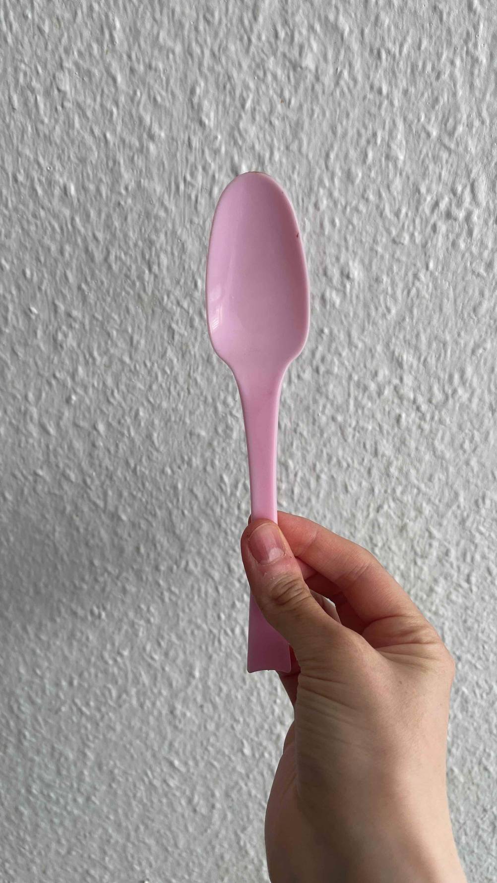 Eine Hand hält einen Plastiklöffel im Test vor eine helle Wand.