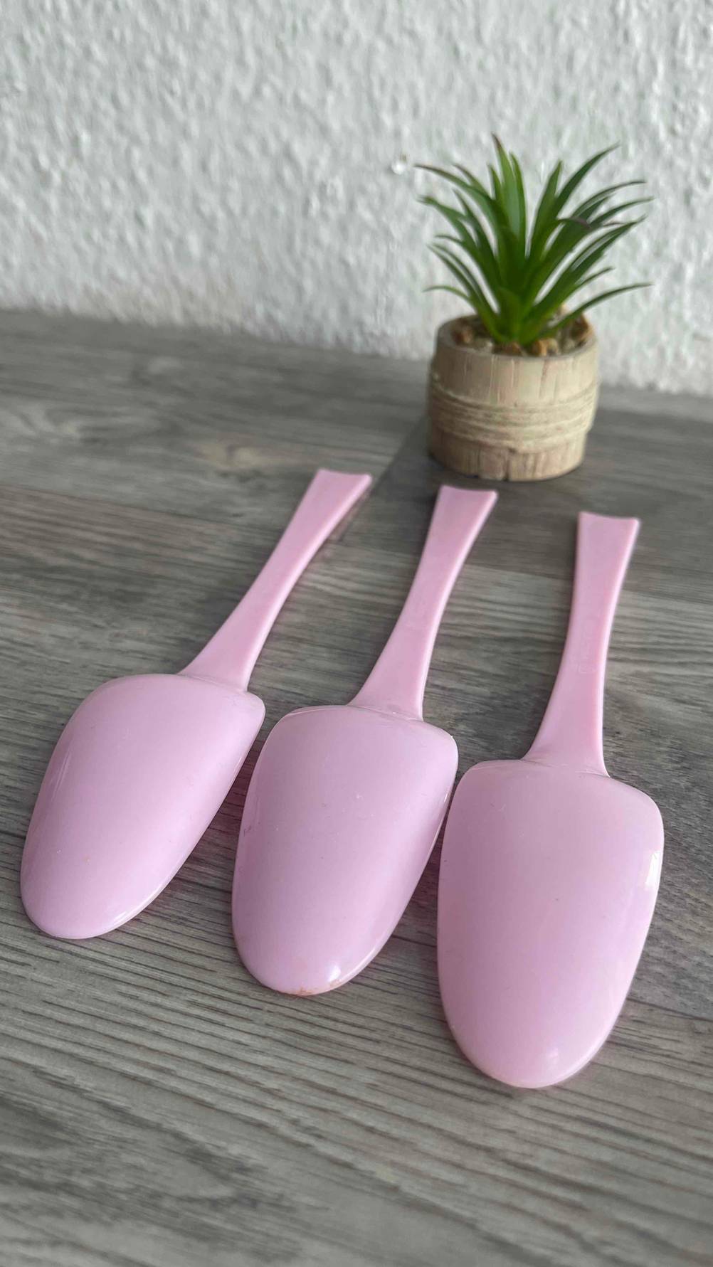 Drei der getesteten Plastiklöffel liegen mit der Rückseite nach oben auf einer Holzfläche.