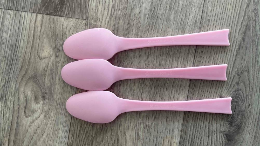 Auf einer Holzplatte liegen drei Plastiklöffel im Test mit der Rückseite nach oben.