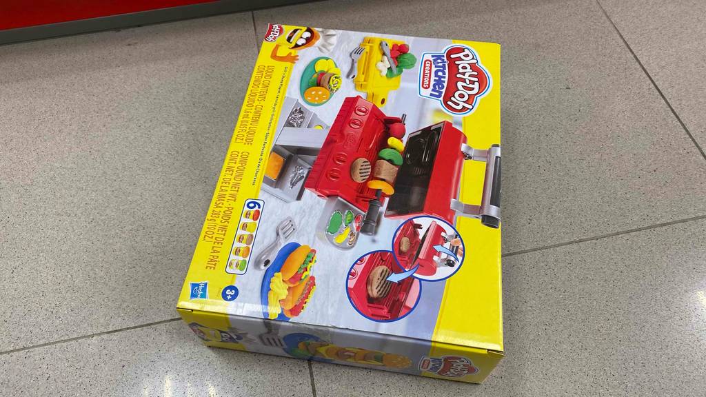 Originalverpackung eines getesteten Play Doh Kindergrills liegt hochkant auf einem Fliesenboden.