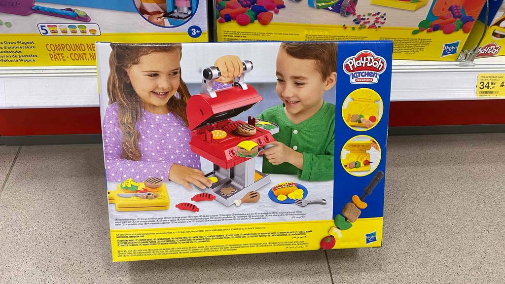 Ein Originalkarton mit Play Doh Kindergrill steht zum testen vor einem Regal.
