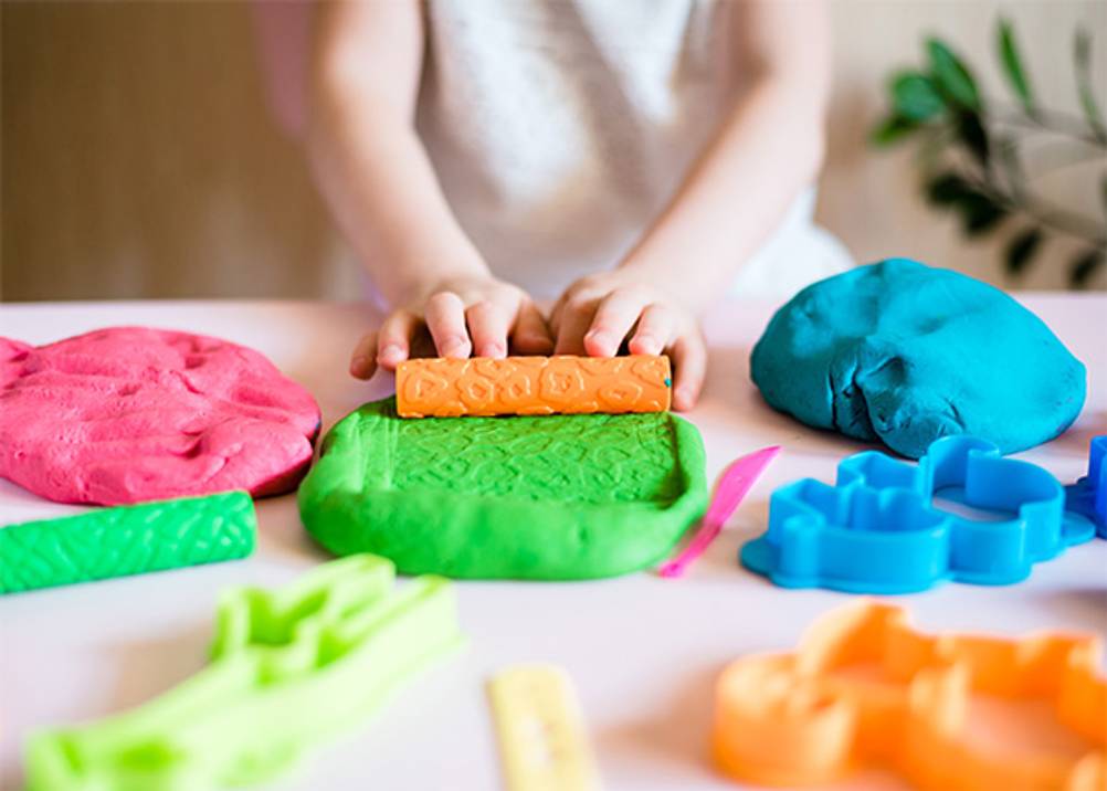 Play-Doh im Test: Kinderhände, die eine grüne Knete mit einem Muster versehen.