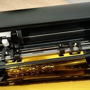 Im Plotter von Silhouette America werden testweise Schneeflocken aus goldener Folie ausgeschnitten.