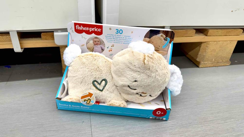Auf dem Boden vor einer Holzpalette steht der Plüschhase im Test in der Verpackung.