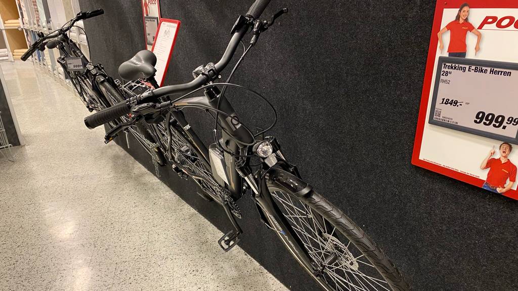 Trekking-E-Bike Herren Gesamtansicht eines E-Trekkingbikes für Herren im Test, das in einem Verkaufsbereich inklusive Preistafel steht.