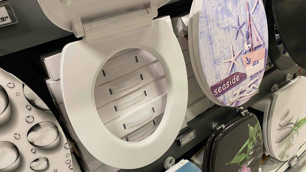 Zum Testen: Ein an einem Regal hängender WC-Sitz mit Ansicht der WC-Brille bei geöffnetem Deckel.