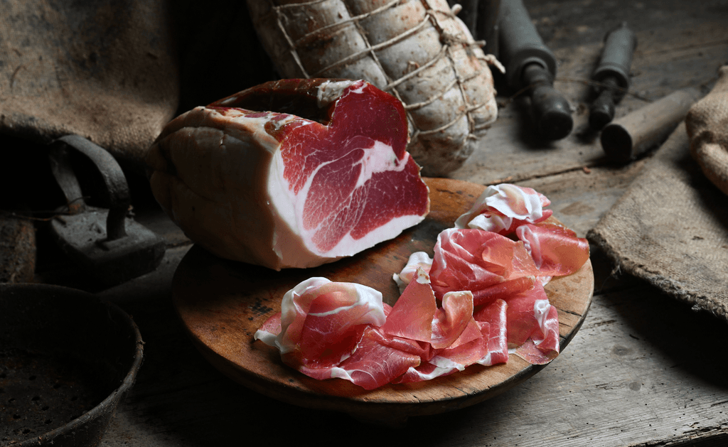 Pökelsalz-Test: Auf einem Holzbrett befindet sich ein Stück Speck und aufgeschnittene Speckscheiben. 