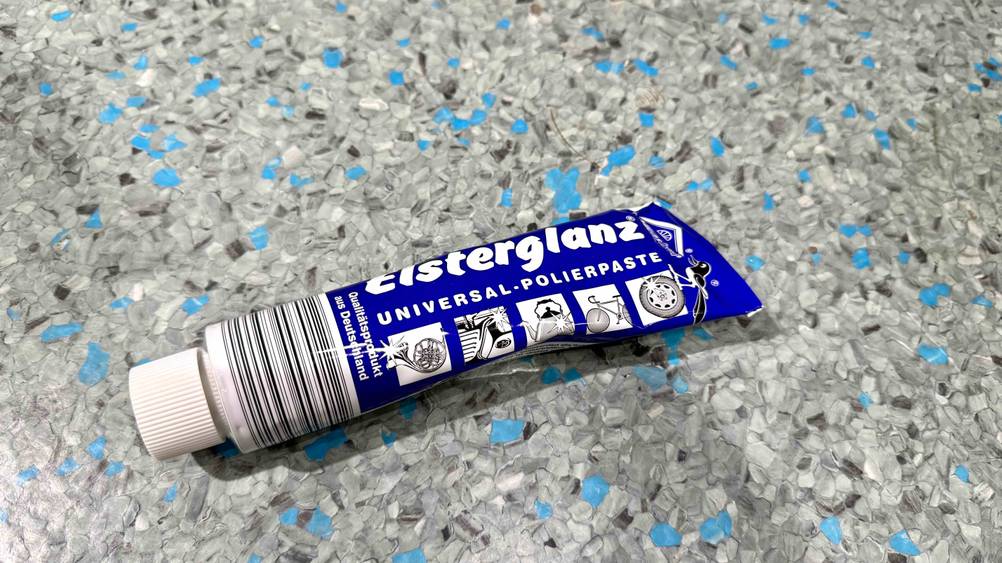 Auf einem grau-blauen Boden liegt eine Tube der Polierpaste im Test.