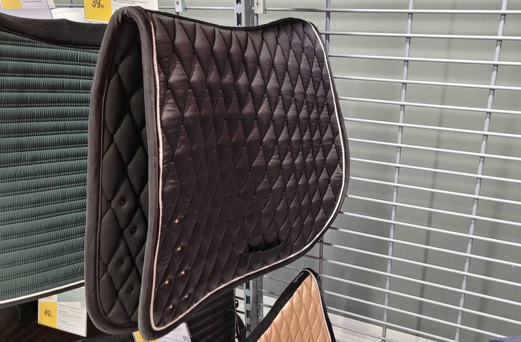 Ein getestetes Fouganza Schabrackensattelpad hängt in einem Regal.