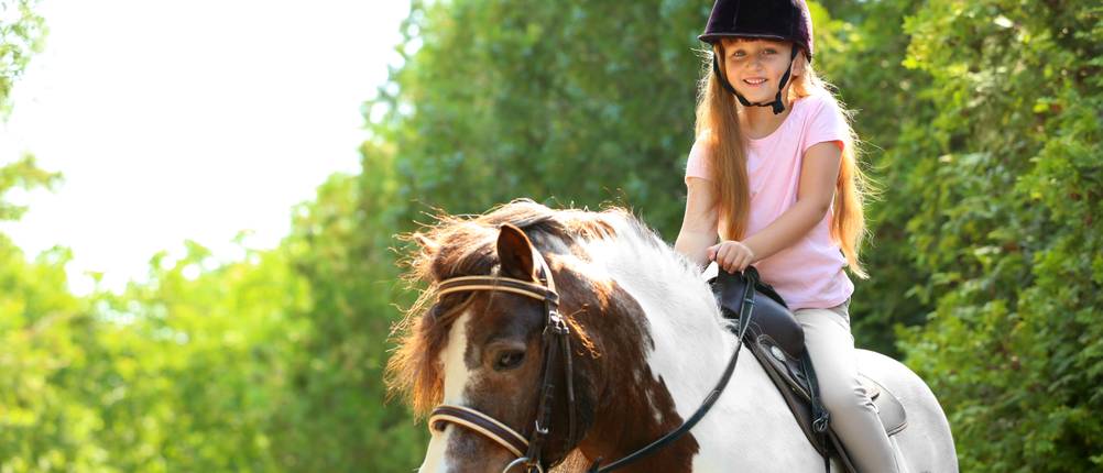 Ponysattel-Test: Ein Mädchen mit Reithelm reitet auf einem Pony.