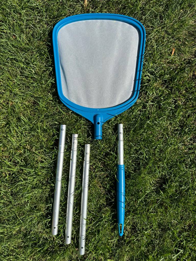 Im Test: ein Pool-Kescher mit verlängerbarem Teleskopstiel liegt auf einem Rasen.