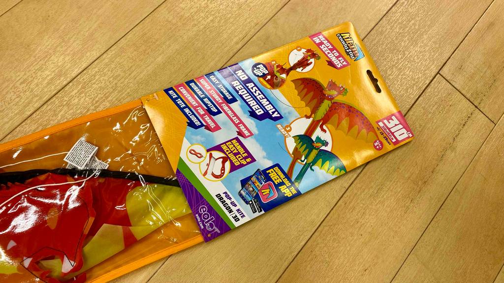 Getesteter Kinderdrachen: Detailansicht der Vorderseite einer Originalverpackung, die auf einem Holzboden liegt.