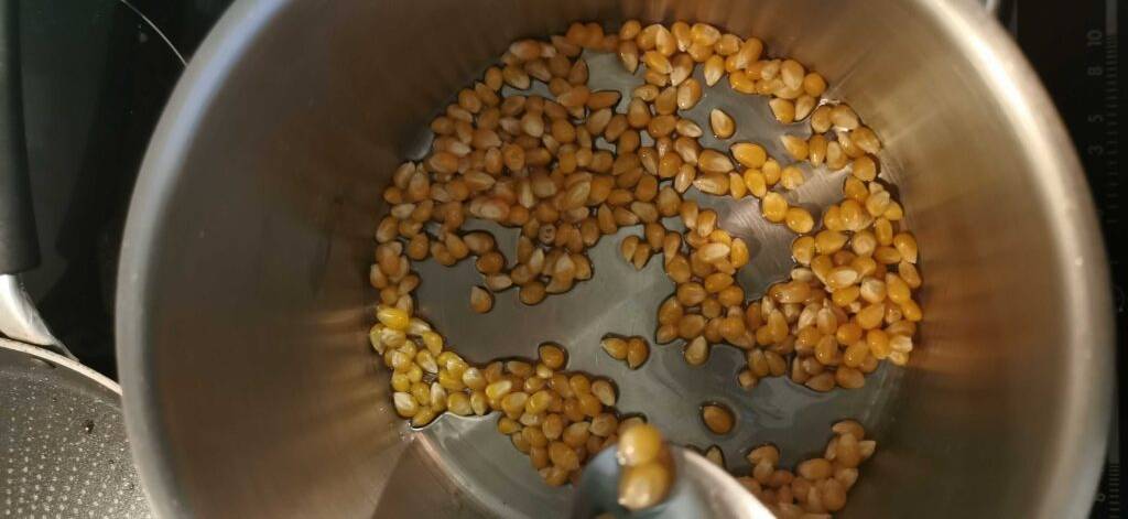 Getesteter Popcornmais liegt in einem Aluminiumtopf inklusive Öl.