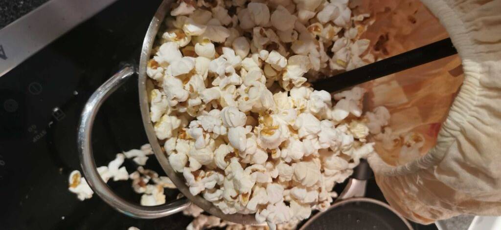 Nahaufnahme von Popcornmais im Test, der sich in einem Topf inklusive schwarzem Rührlöffel und weißem Gummi-Bezug befindet.