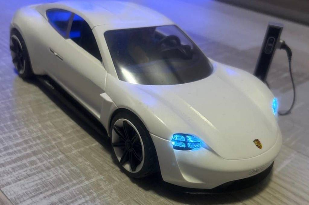 Im Test: Ferngesteuertes Auto im hellen Porschedesign steht mit erleuchteten blauen Scheinwerfern an seiner Miniatur-Ladestation auf einem Boden in Holzoptik.