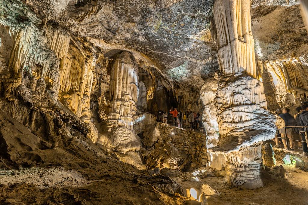 Touristen besichtigen die Postojna-Höhle. Man sieht verschiedenste riesige Stalagmiten und Stalaktiten.