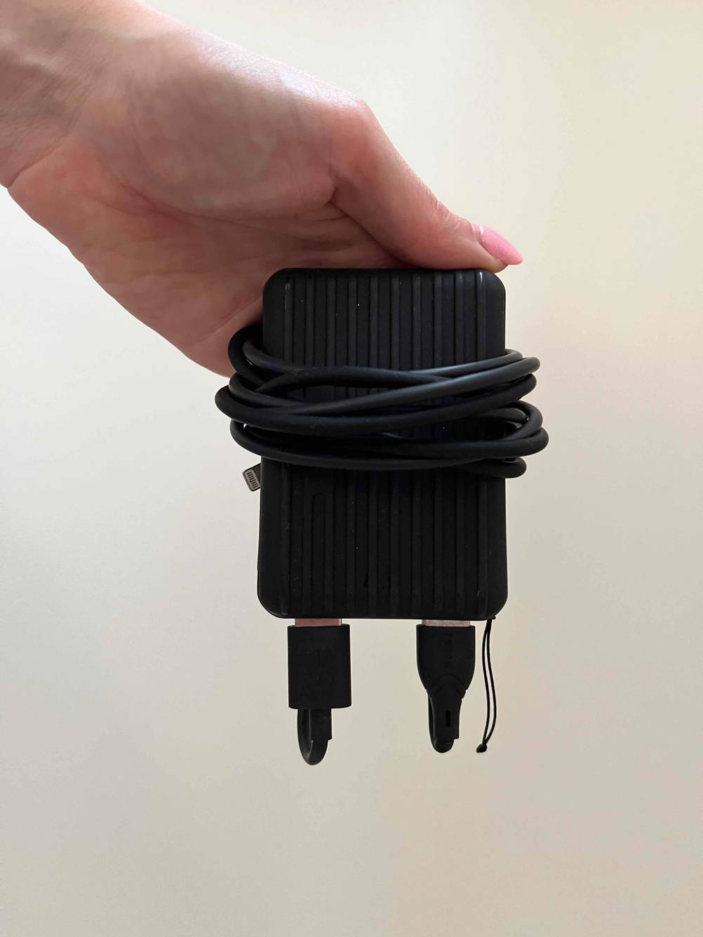 Powerbank 10.000 mAh getestet: Eine Hand hält ein Gerät mit Kabeln umwickelt vor einer helle Wand.