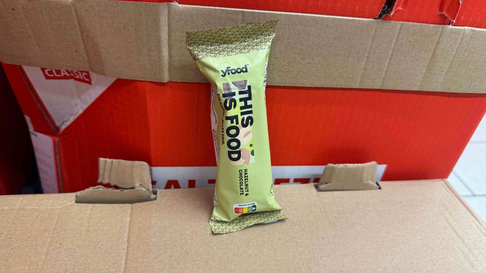 Auf einem Karton lehnt ein getesteter Powerbar Riegel an einem anderen Karton.
