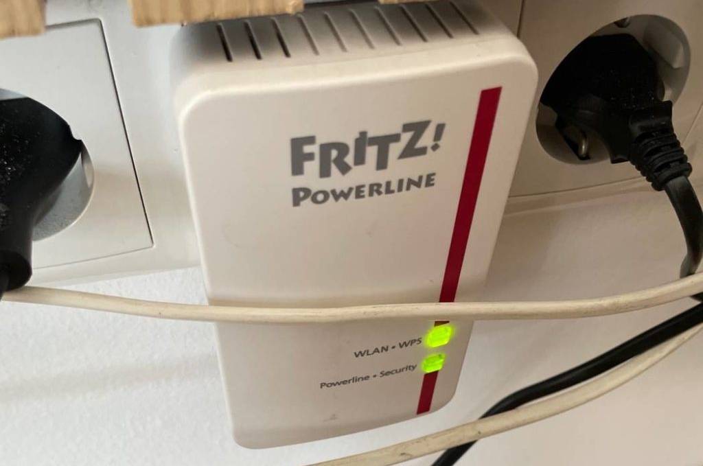 Access Point im Test: Die weiße Powerline-WLAN-Erweitertung von AVM Fritz befindet sich in einer Steckdose oberhalb der Fußboden-Fußleiste aus Holz.