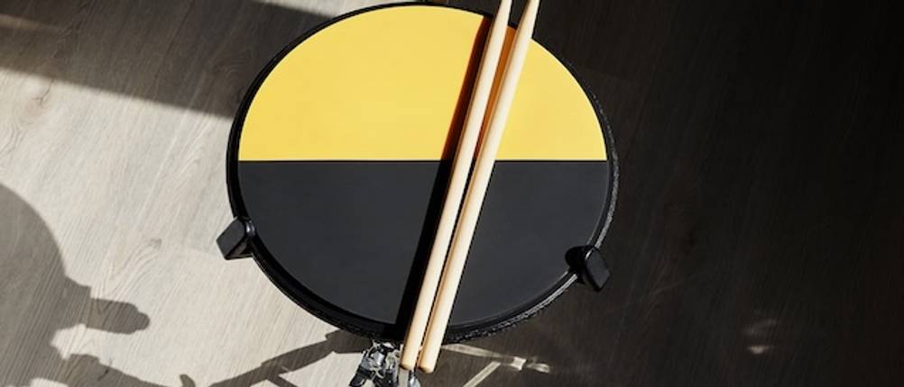 Ein gelb-schwarzes Practice-Pad mit Drumsticks von oben auf einem Ständer.
