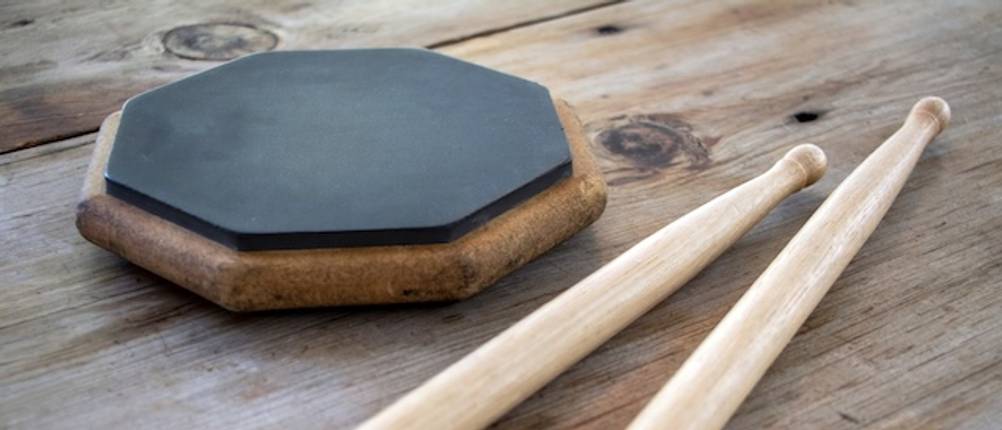 Practice-Pad-Test: Ein Übungspad aus Holz mit einem Gummitrommelfell liegt gemeinsam mit Schlagzeugsticks auf einer Holzfläche.