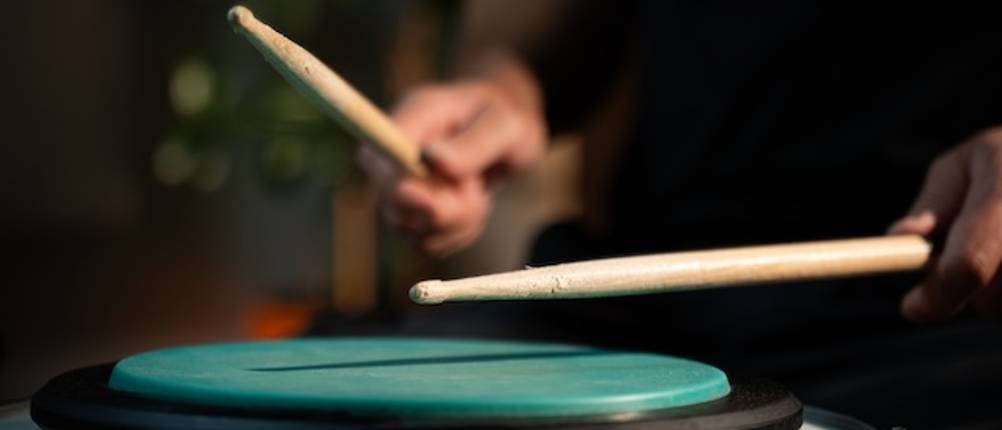 Ein Mann testet ein grünes Practice-Pad mit Schlagzeugsticks.