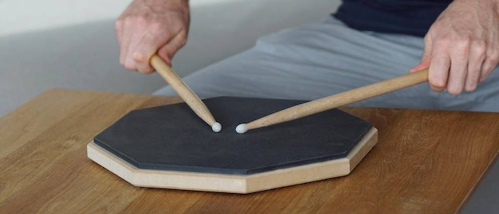 Ein Mann testet ein Practice-Pad mit Drumsticks.
