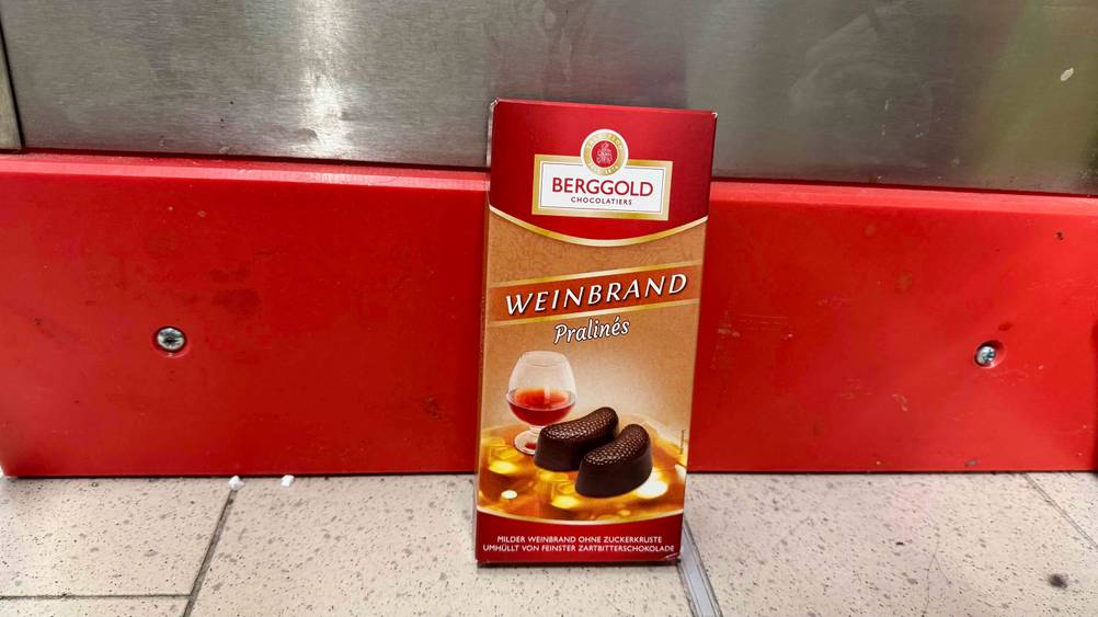 An einer roten Leiste lehnt eine Packung der getesteten Pralinen mit Alkohol.