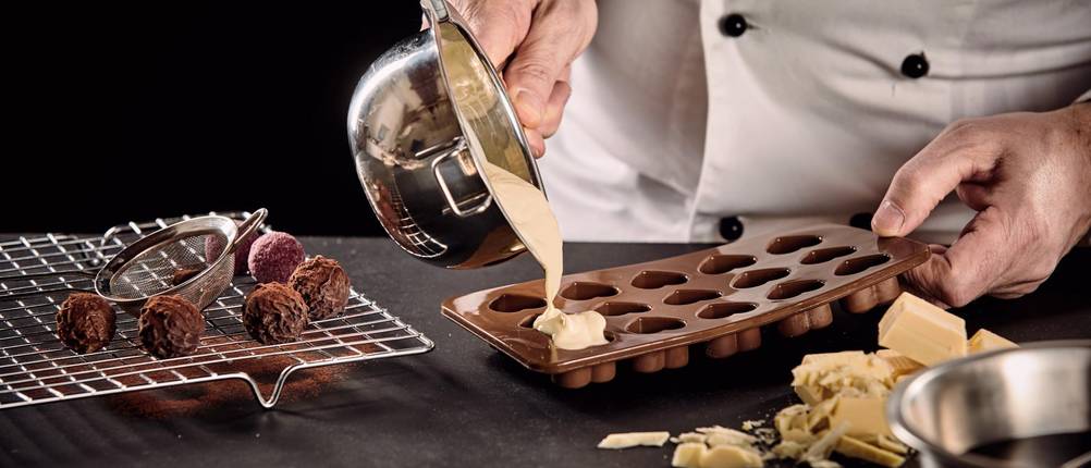 Pralinenformen-Test: Chocolatier gießt Creme in Pralinenform.