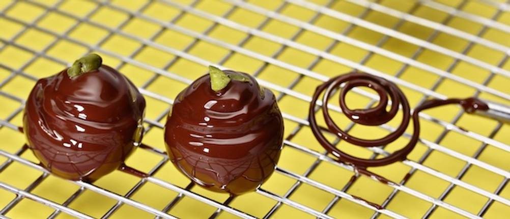 Runde Pralinengabel im Test: Ein Abtropfgitter mit zwei runden Schoko-Pralinen und einer spiralförmigen Pralinengabel.