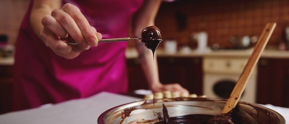 Pralinengabel getestet: Eine runde Pralinengabel mit einer runden von Schokolade überzogenen Praline wird über eine Schüssel gehalten.