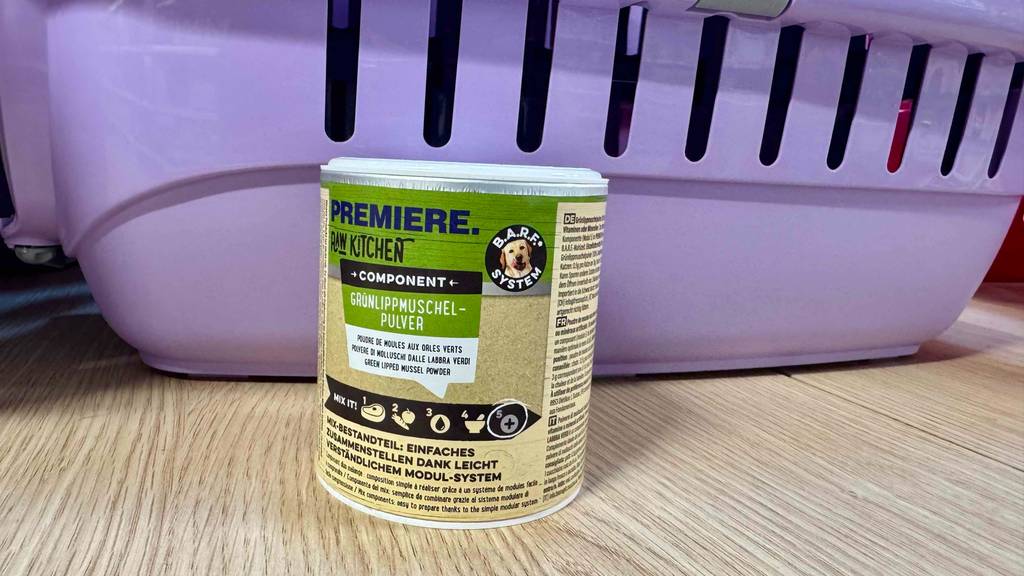 Die Dose mit dem Grünlippmuschelpulver im Test befindet sich vor einem Hundekorb in Violett.