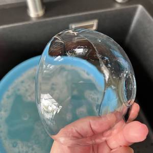 Eine durchsichtige Glasschale wird von einer Hand gehalten. Die Schale ist sauber, jedoch befinden sich noch einige Wassertropfen auf ihr.