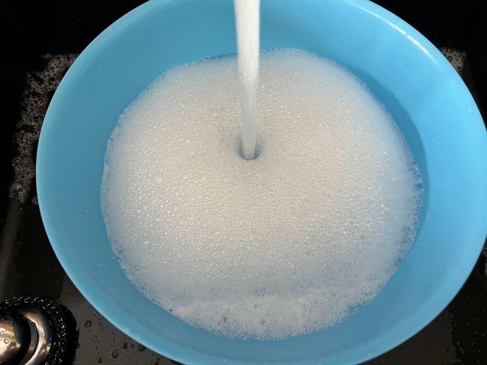 In eine blaue Schüssel läuft Wasser und es entsteht Schaum.