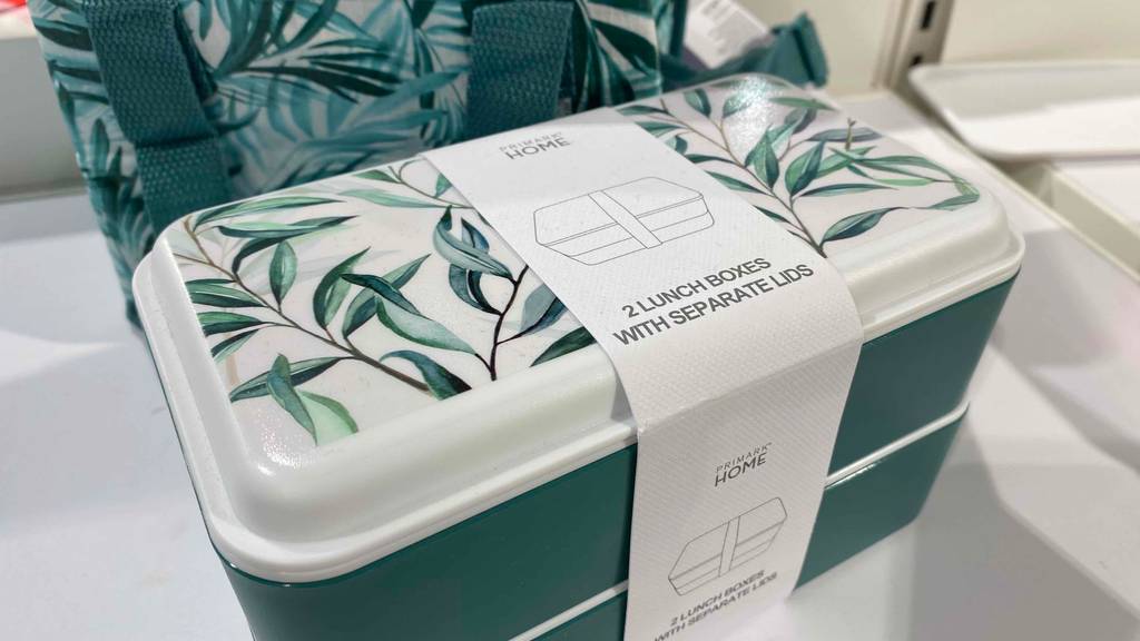 Doppelte grün-weiße Primark Home Lunchbox im Test mit floral designtem Deckel inklusive Pappbanderole steht vor einer Thermo-Tasche.