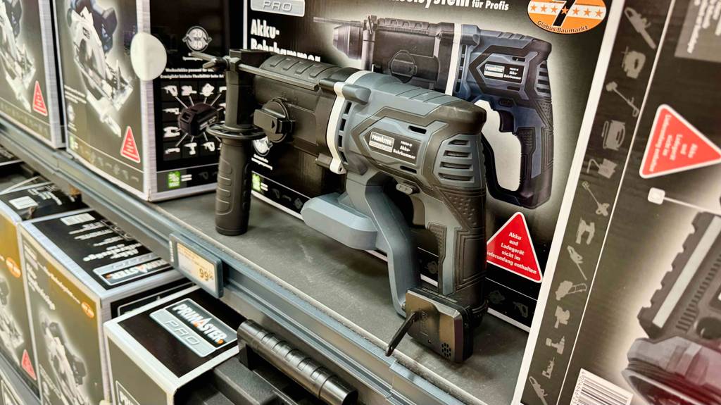 Akku-Bohrhammer-Test: Ein schwarz-graues Modell ohne Akku ist vor seinem Produktkarton in einem Baumarkt ausgestellt.