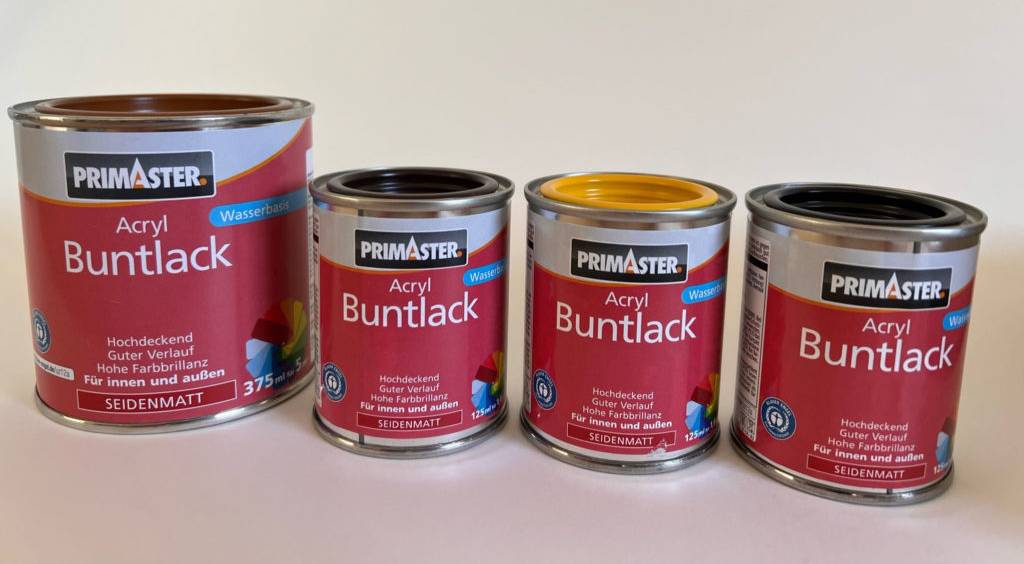 Vier unterschiedlich große Dosen Primaster Maleracryl im Test im roten Design stehen nebeneinander vor hellem Hintergrund.