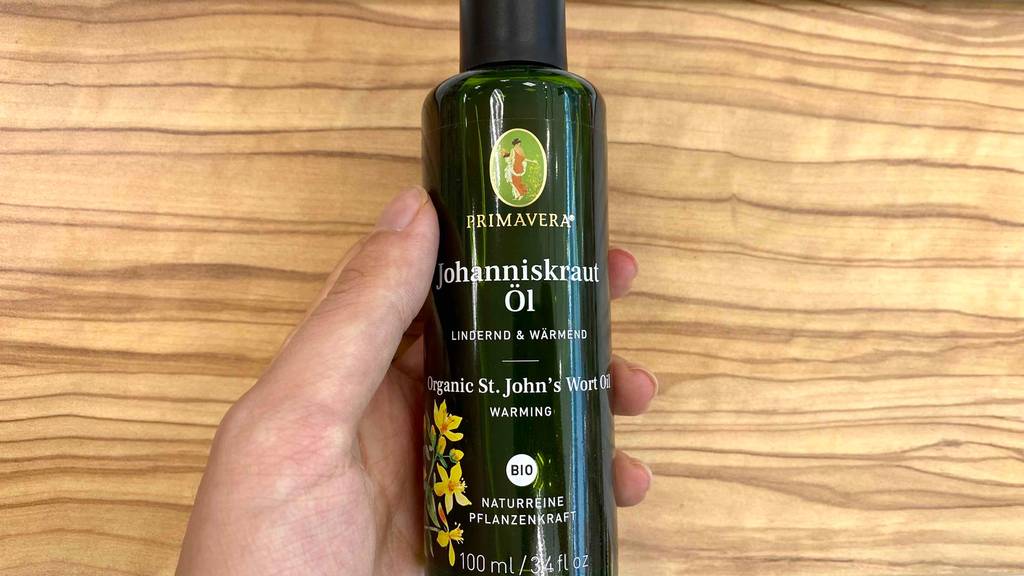 Hand hält getestete Flasche Johanniskrautöl über einem Holztisch.