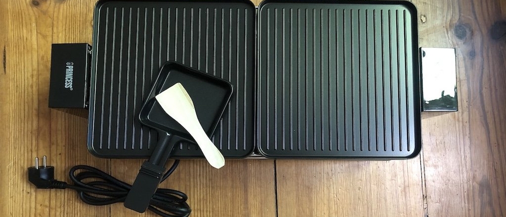 Raclette-Test: Vollaufnahme eines dunklen Raclettes von Princess mit zwei Grillflächen, Pfännchen und Schaber. 