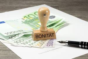 Privatkredite im Test: Ein Stempel mit dem Schriftzug Bonität steht auf einigen Geldscheinen, während daneben ein Füller liegt.