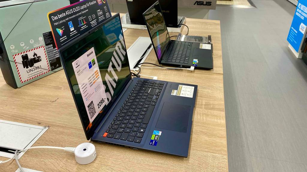 ASUS-VivoBook im Test: Seitenansicht auf ein schwarzes Modell inklusive Preisschild und Produktinformationen, das auf einem Holztisch im Verkauf steht.