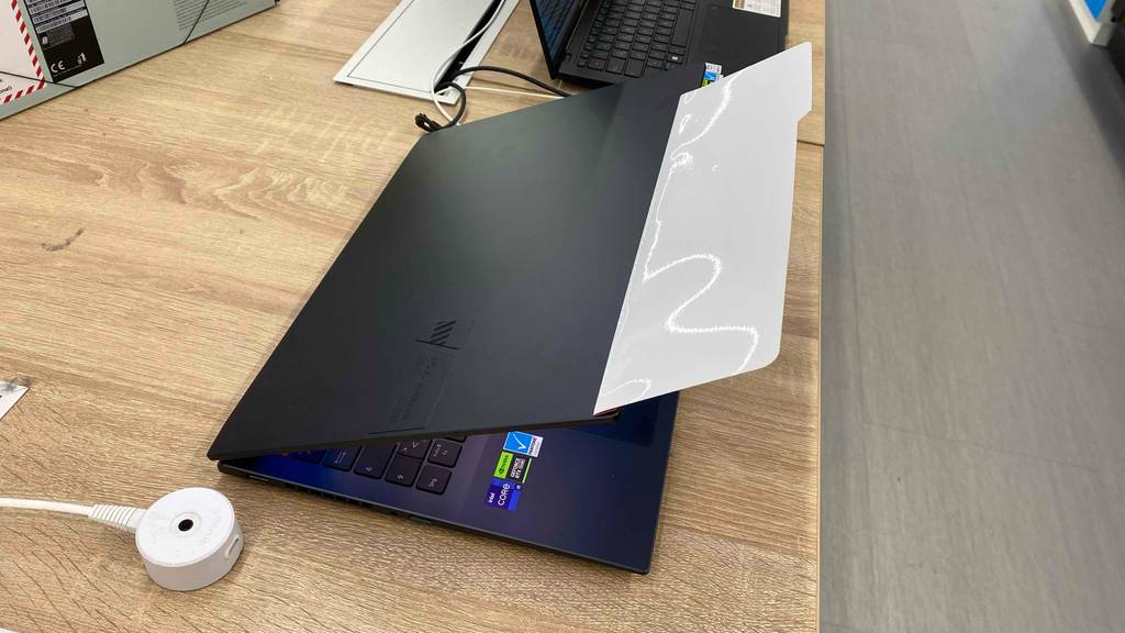 Ansicht von schräg oben auf ein schwarzes ASUS-VivoBook im Test, das mit leicht geschlossenem Bildschirm auf einem Holztisch im Geschäft steht.