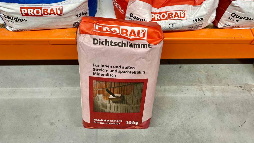 Verpackung der getesteten Dichtschlämme steht auf grauem Untergrund.