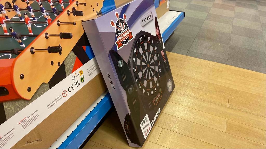 Eine verpackte Dartscheibe steht zum Testen vor einem Regal mit anderen Geräten.