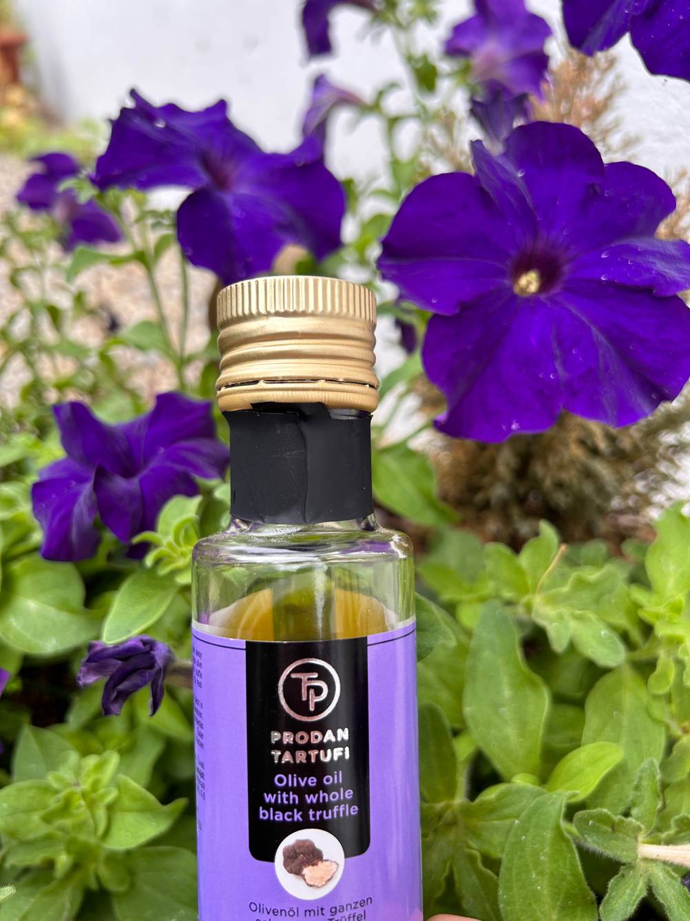 Trüffelöl im Test: Detailansicht Verschluss einer Flasche, die vor lila Blumen steht.