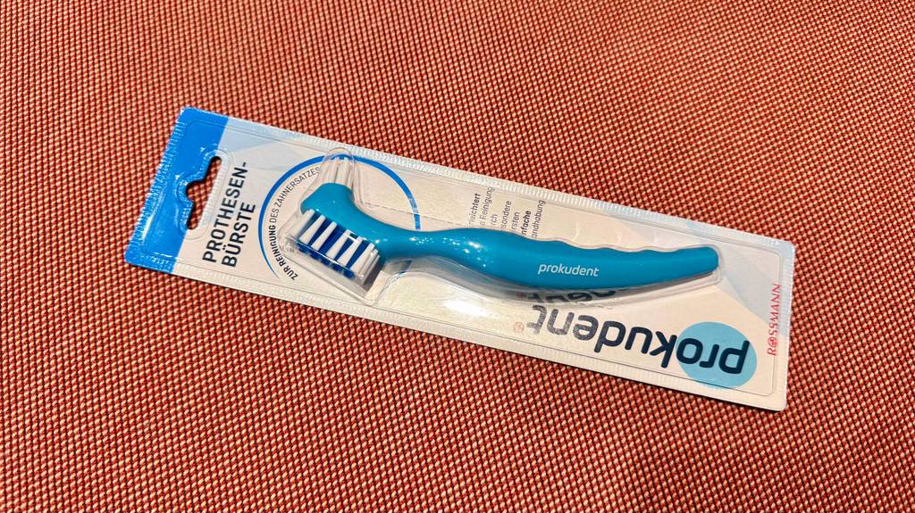 Getestet: Eine Prothesenbürste in der Verpackung liegt auf einem roten Untergrund.