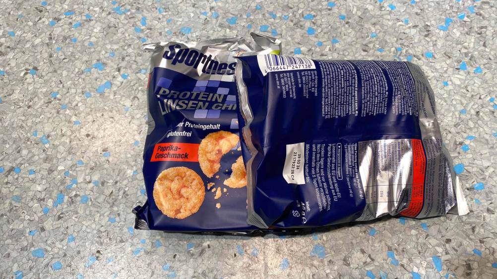 Auf dem Boden befinden sich zwei Packungen getestete Protein-Chips mit Nährwertangaben. 