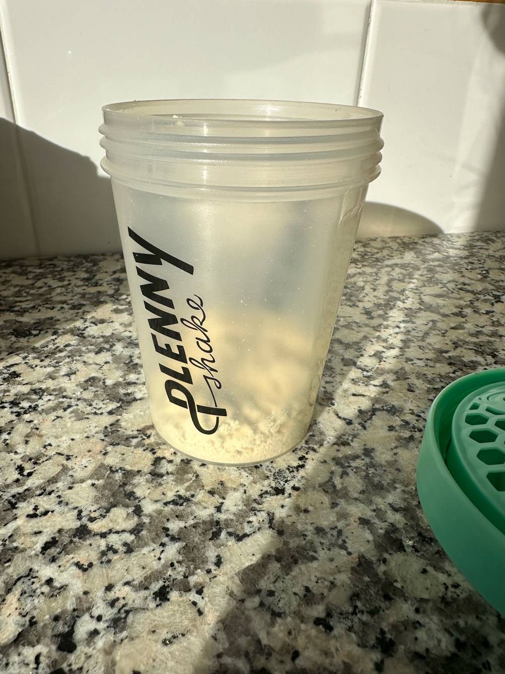 Ein offener zum Teil mit Pulver gefüllter Becher eines getesteten Eiweiß-Shakers steht auf einer Arbeitsplatte.