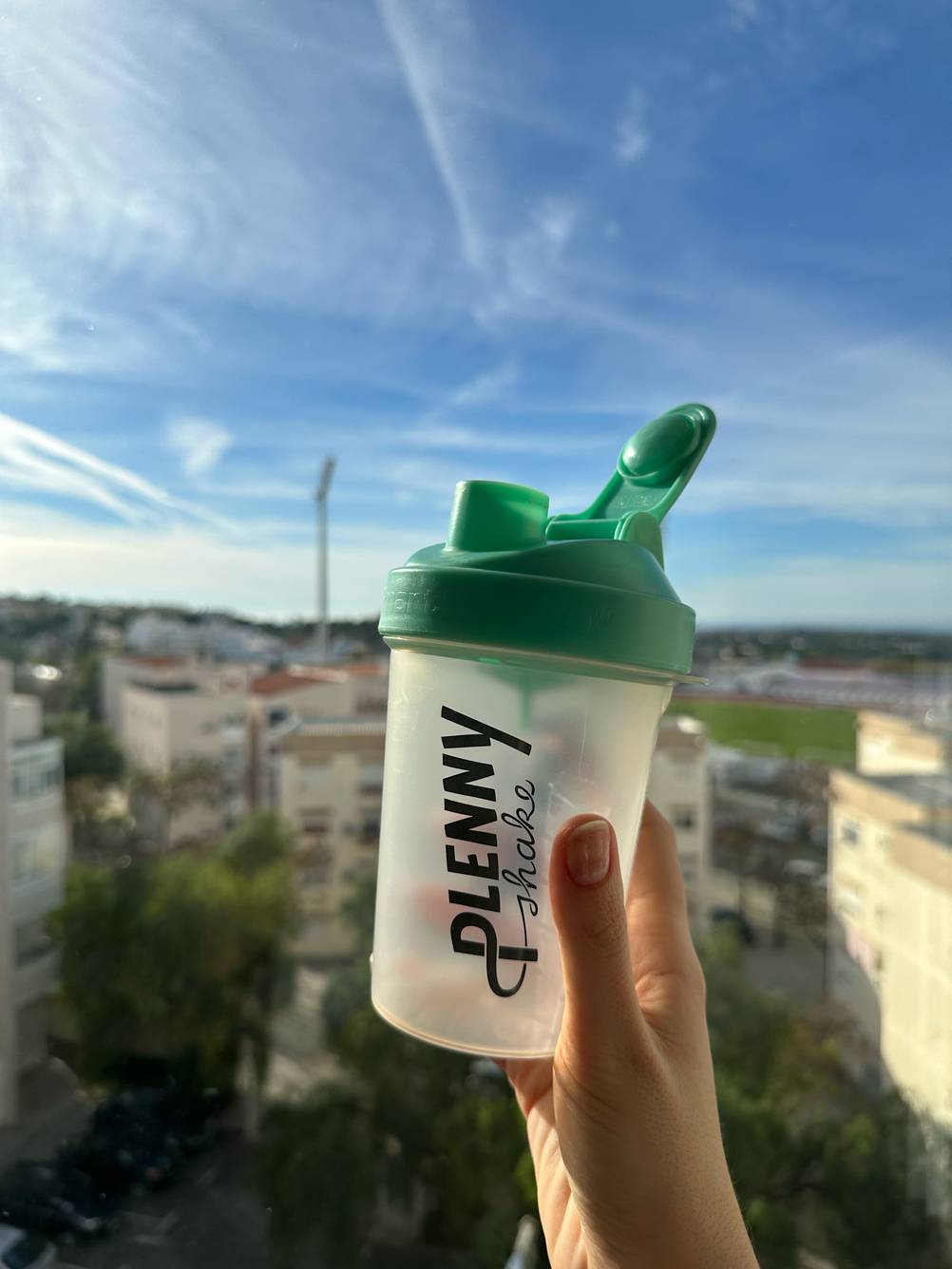 Hand hält einen getesteten Eiweiß-Shaker mit geöffnetem Trinkloch in den Himmel.