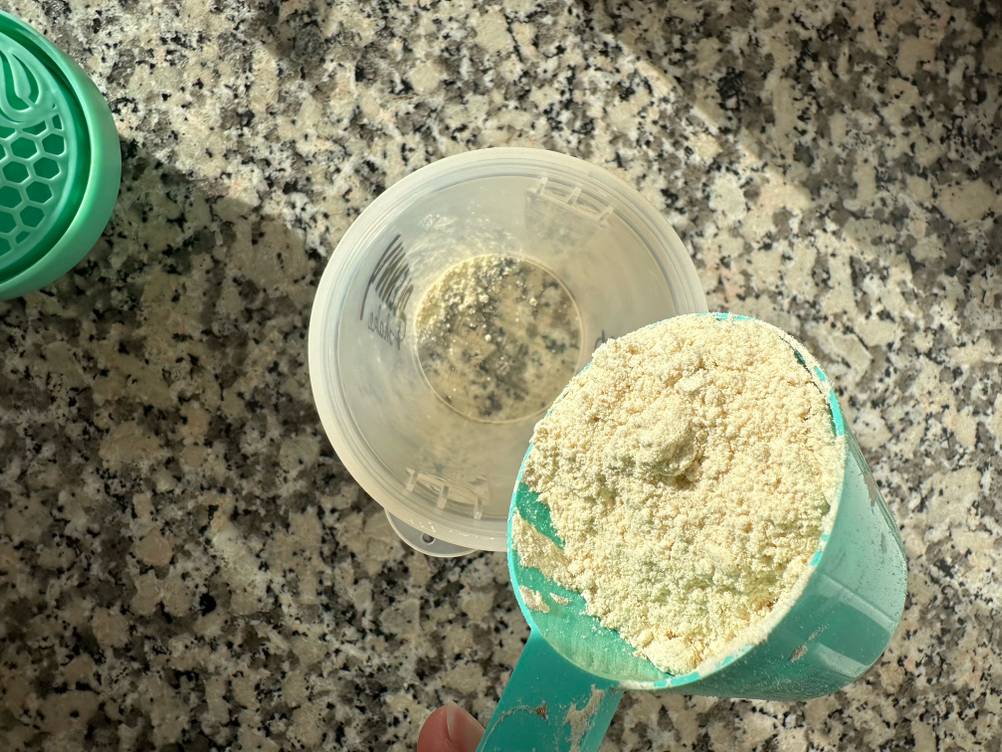 Eiweiß-Shaker-Test: Ein gefüllter Dosierlöffel wird in den offenen Becher geschüttet.